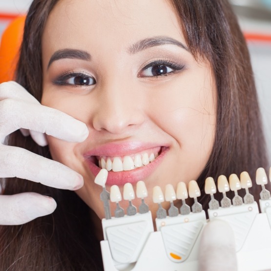 Young woman smiling next to row of dental veneers