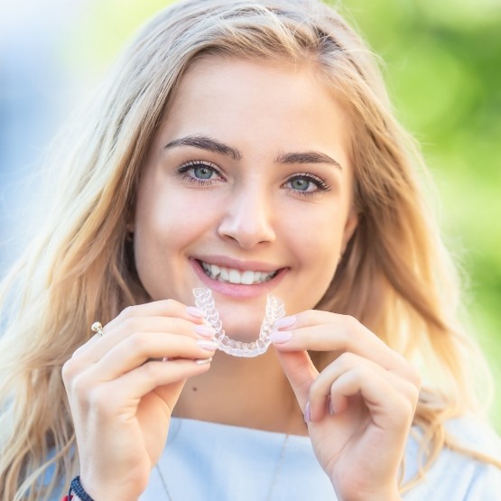 Smiling blonde woman holding an Invisalign tray