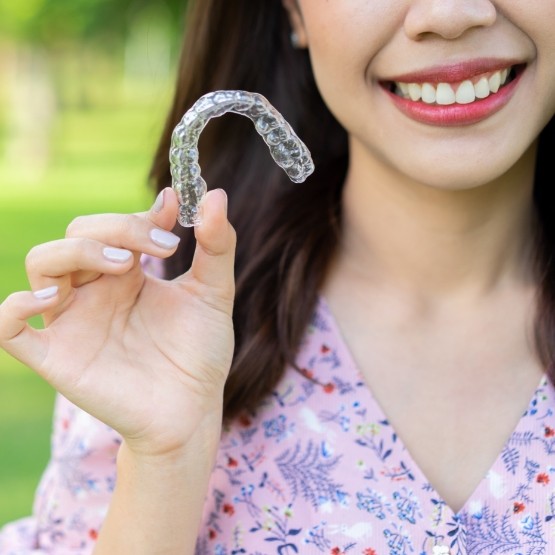 Smiling woman holding an Invisalign clear aligner