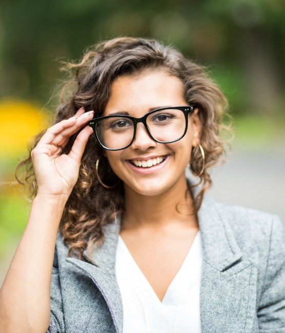 Smiling young woman holding her glasses after restorative dentistry