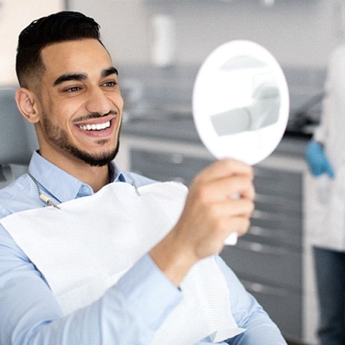 Man smiling at reflection in handheld mirror