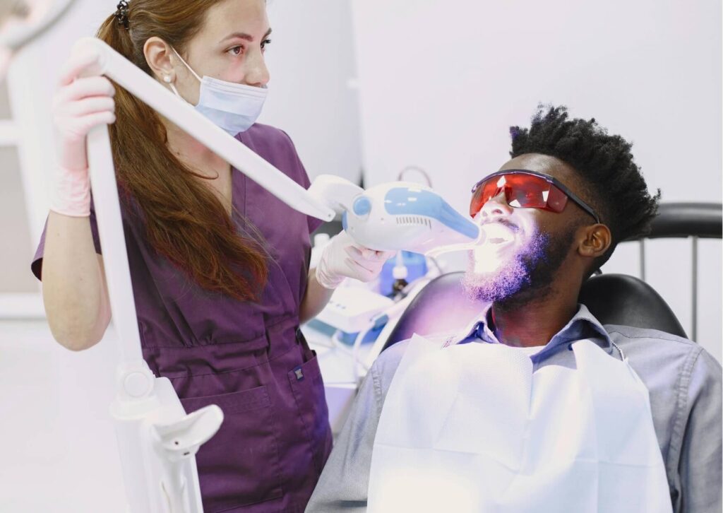 Patient receiving professional teeth whitening treatment with LED whitening light during an in-office dental procedure